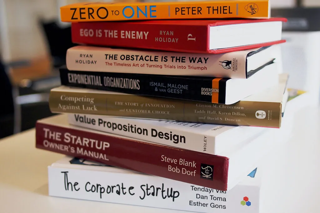A stack of business and founder books from The Native Library — Zero to One, Ego Is the Enemy, The Obstacle Is the Way, The Startup Owner's Manual and more